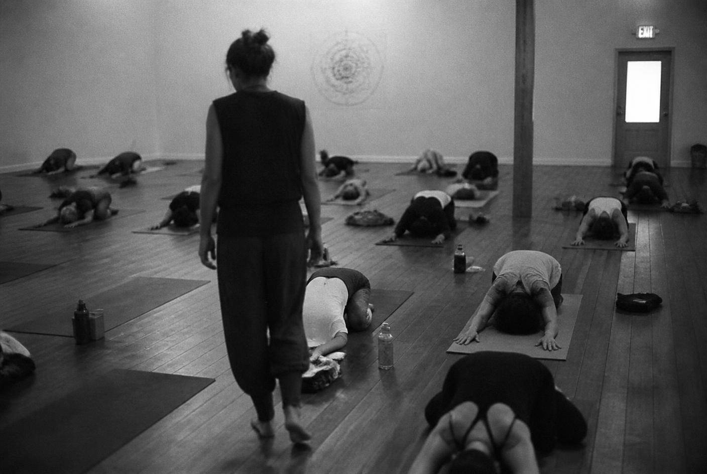 A teacher walking through a studio observing students resting on their mats